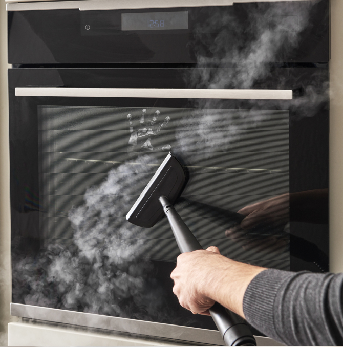 Un limpiador a vapor limpiando el espejo de un horno