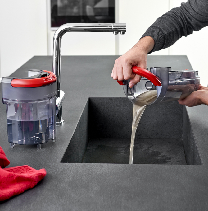 Un hombre tirando un tanque de agua sucia en un fregadero.